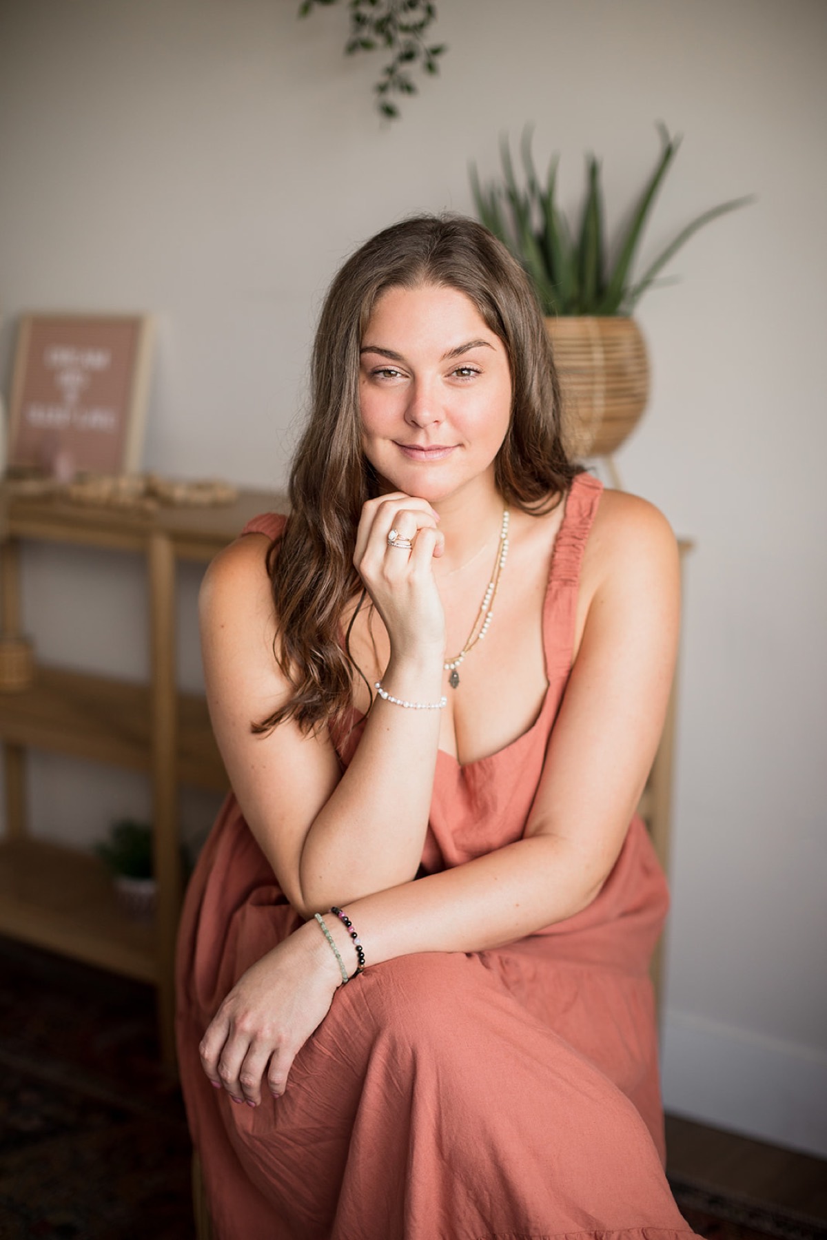 Heather Flynn in a coral dress, smiling warmly in a sunlit studio with plants and crystals